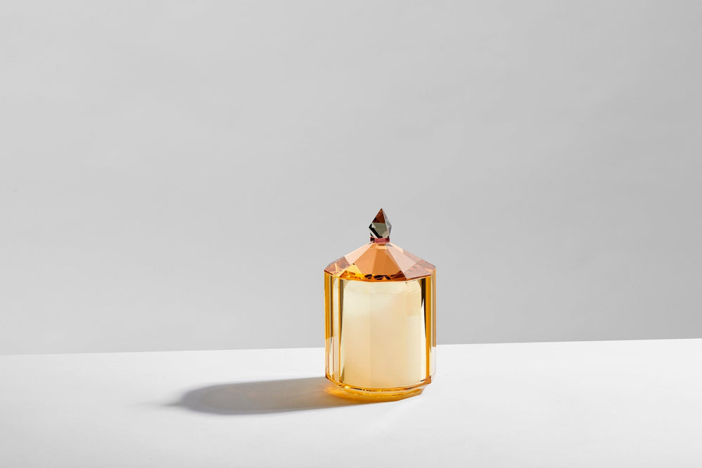 Doftljus i en behållare av gul kristall, på ett vitt bord och med grå bakgrund