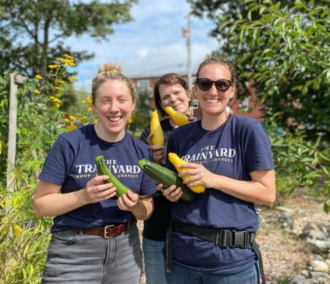 Rachel, Kelly & Kim stand in the garden at The North Grove wearing blue Trainyard shirts and holding zucchini