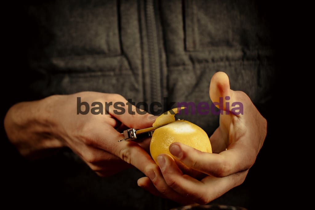 Bartender peels orange peel for cocktail at bar Stock Photo by