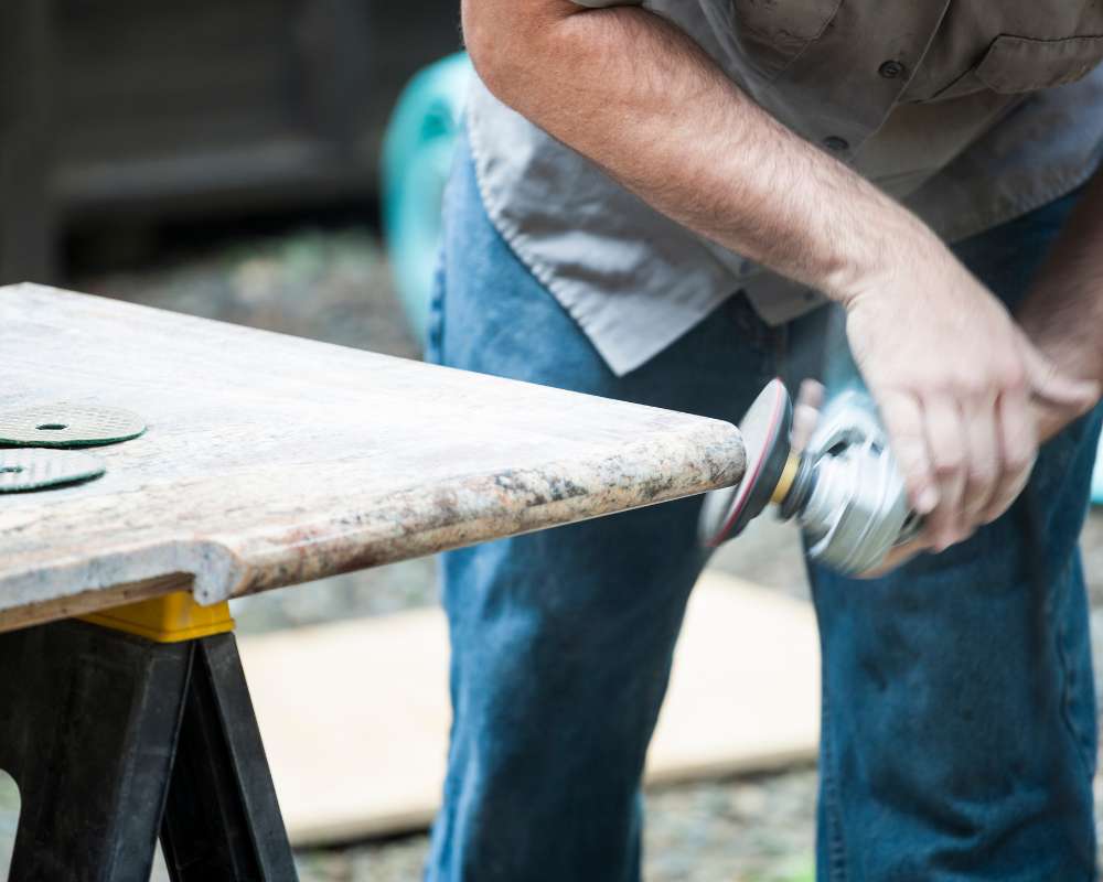 Granite countertop being polished by a handyman using an angle grinder and diamond abrasive pads