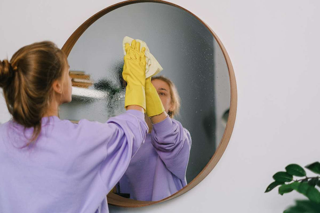 Es ist eine Heimwerkerin zu sehen die den Spiegel nach dem Befestigen putzt und versiegelt.