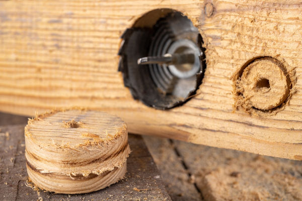 Ein Loch wird durch das Holzbrett gebohrt mit Bohrmaschine und Holzlochsäge