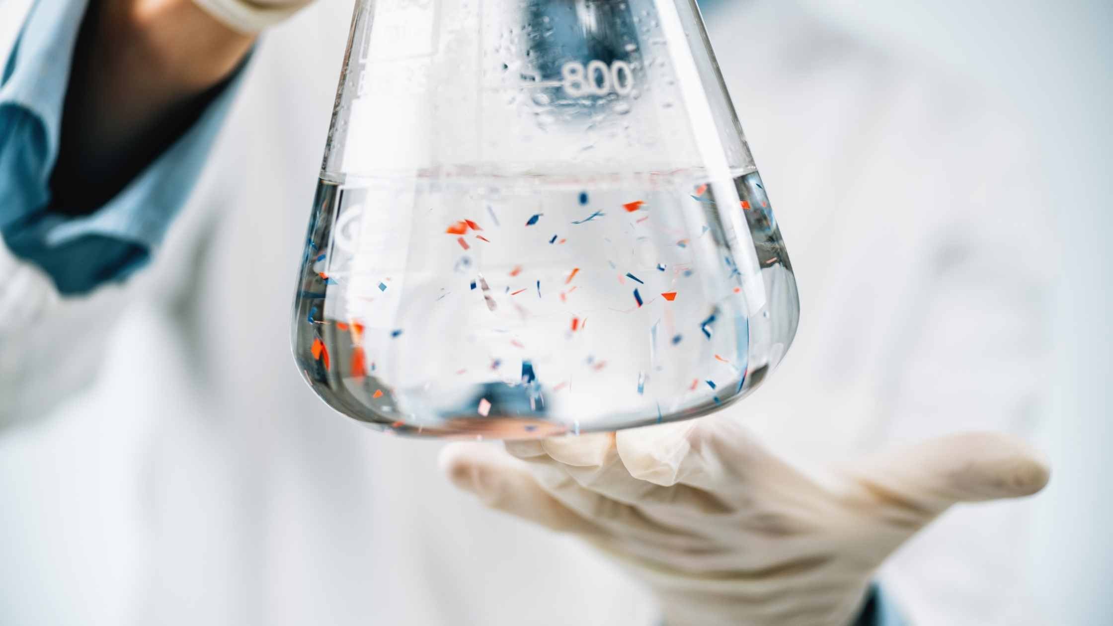 Plastic-free Image of beaker with water and microplastics held by gloved handed scientist in lab coat