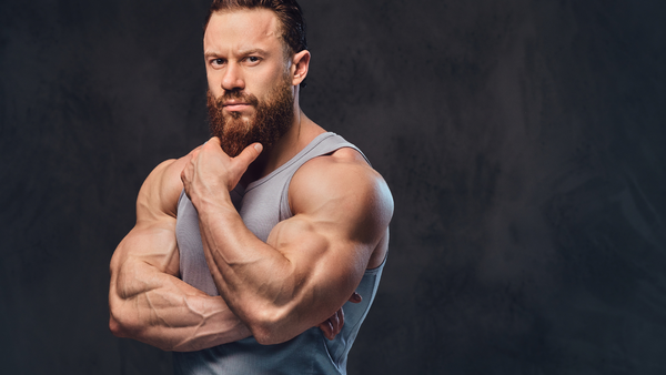 A professional weightlifting athlete who is very muscular poses with a tank top and looks on with a contemplating look.