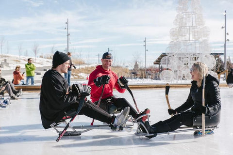 Photo of Ryan Straschnitzki, Chris Cederstrand, and Tara Nelson sitting in sledge hockey sledges on ice.