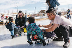 Photo of U of C volunteer helping a child get into a sledge hockey sledge.