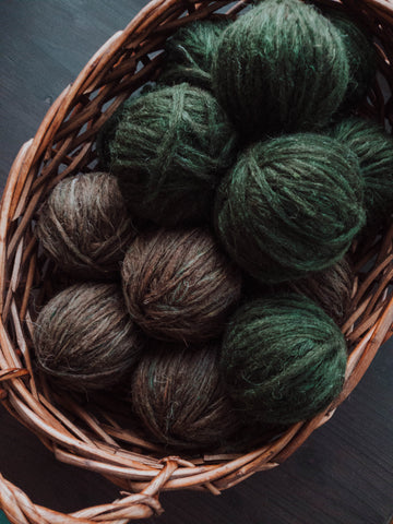Balls of unspun Nutiden and Plötulopi yarn of various green shades in a basket. 