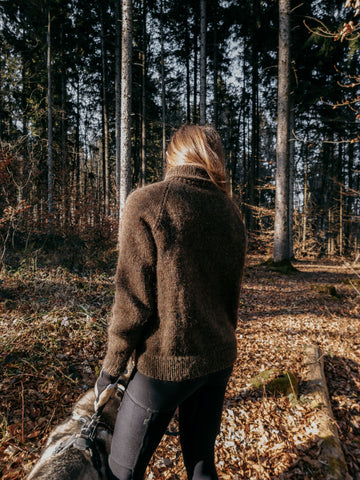 The knitwear designer with her husky in a sunny autumnal forest wearing Lo-ki Raglan Sweater. 