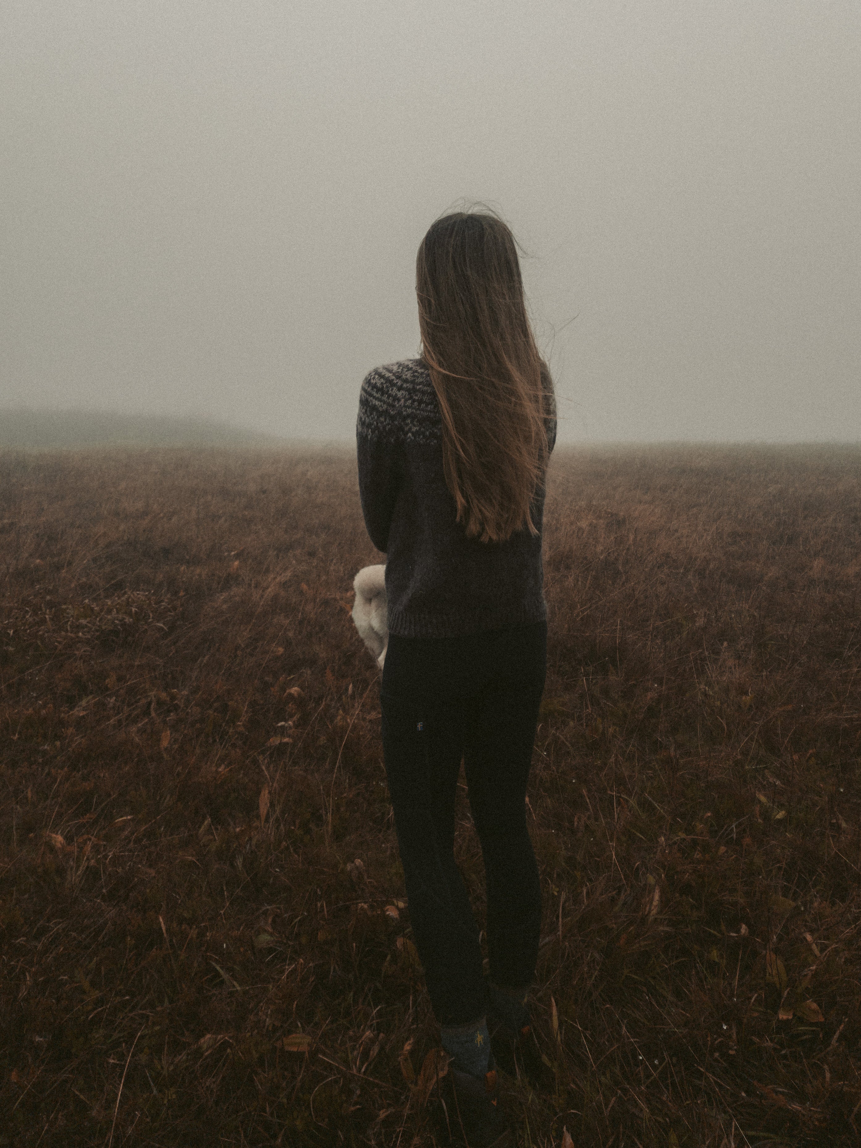 Knitwear designer standing in foggy, windy field wearing Barren Land Sweater.