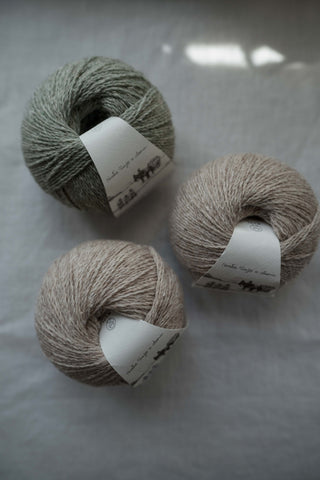 Three balls of Saona yarn by Wooldreamers displayed on a natural linen cloth on a table.