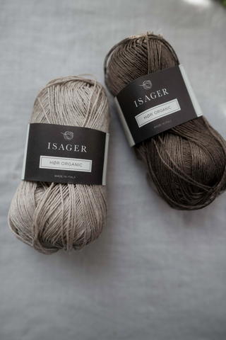 Two balls of linen yarn - Isager HØR ORGANIC displayed on a natural linen cloth on a table.