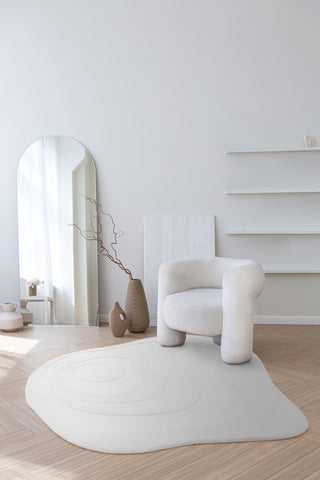 A Minimaluxe room featuring elements of luxury and Minimilasm. There is an irregularly shaped white rug with soft curved edges and a textured wavy design inside. The rest of the décor is sophisticated and also features curved areas. The room is mostly white but features some warmer brown tones in the floor.