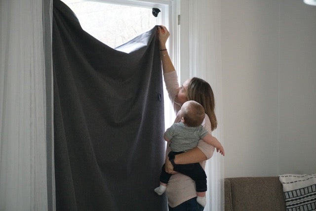 Mother putting up blackout curtains while holding a baby