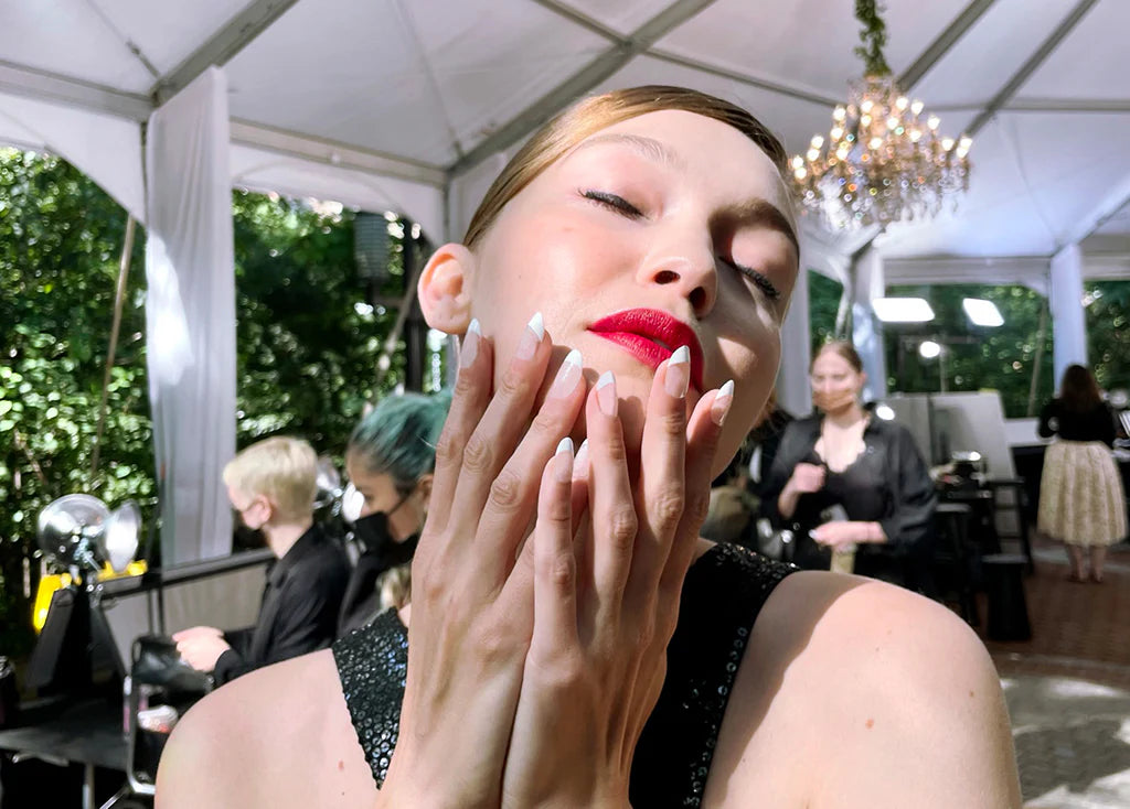 Model with red lipstick caressing her face with her hands: Almond/Round Shaped Nails