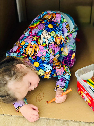 Little girl wearing a rainbow coloured jumper while colouring on cardboard