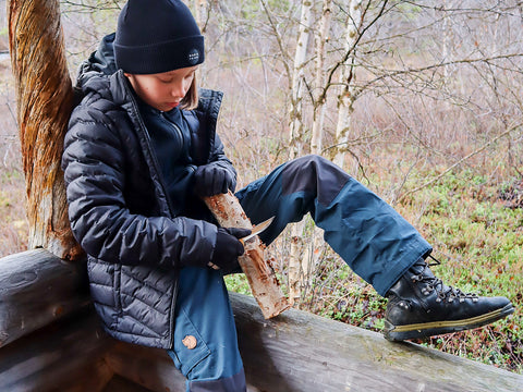 nachdenklich - der Junge sticht mit einem Messer auf einen Baum im Wald