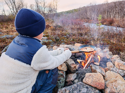 Der Junge röstet am Lagerfeuer in der Natur Lapplands eine Linguine, obenauf die von Olkia verkauften Produkte