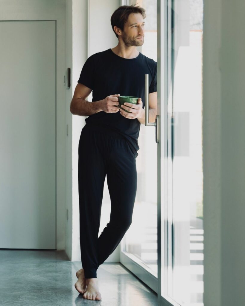 man indoors with cup in hand wearing black t-shirt