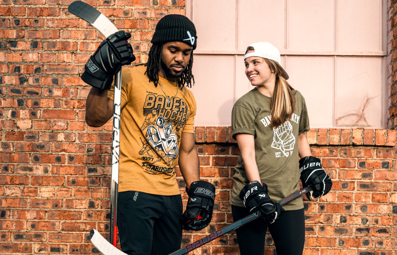 two people holding various roller hockey equipment with a brick wall in the background