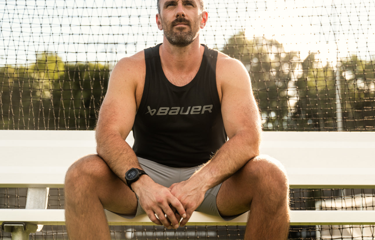 man sitting on bleachers in tank top and exercise shorts