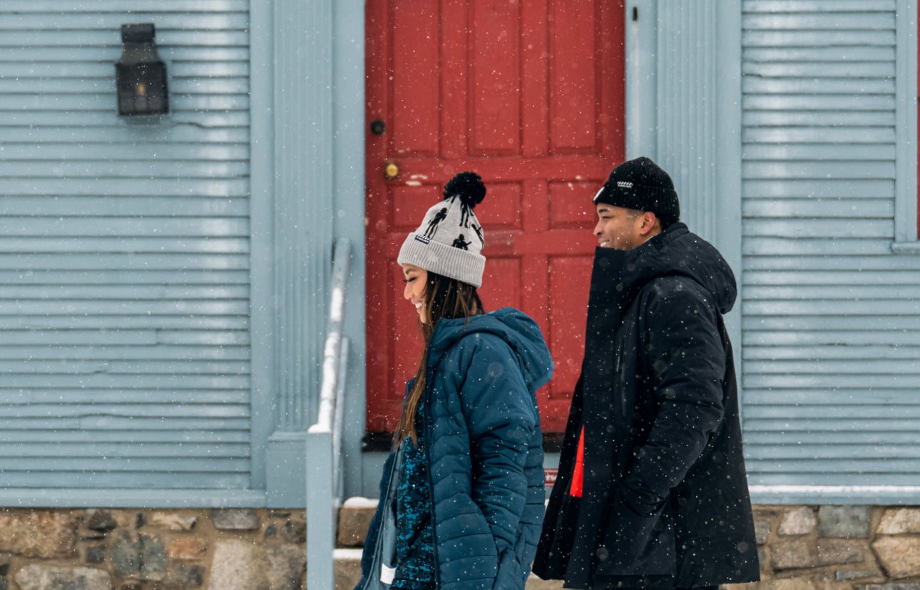 man and woman walking by a red building in winter coats and hats