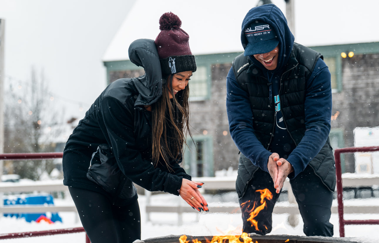 two people wearing winter apparel warming their hands over an outdoor fire pit