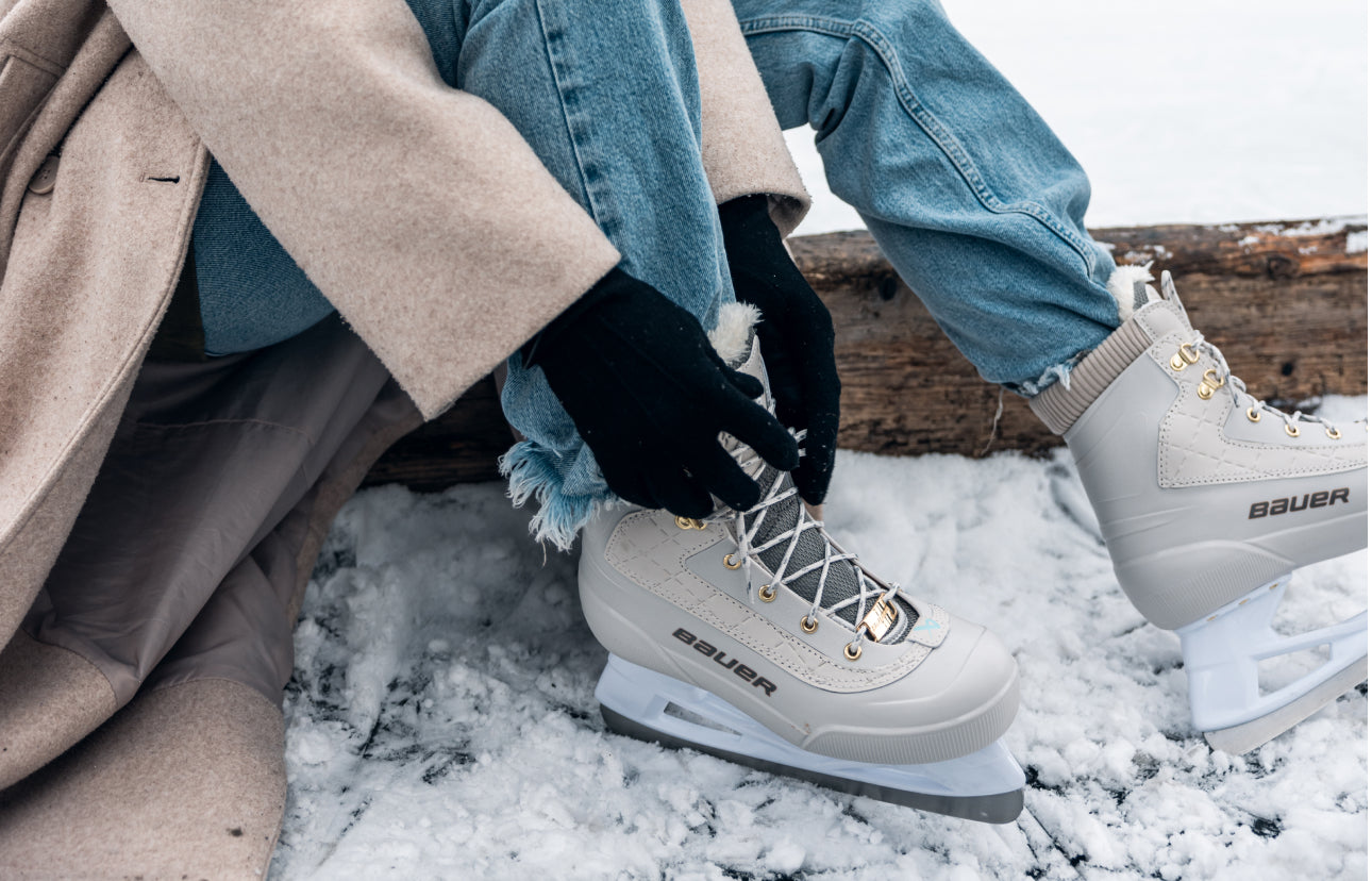 close up of person sitting on ice lacing up a white pair of ice skates
