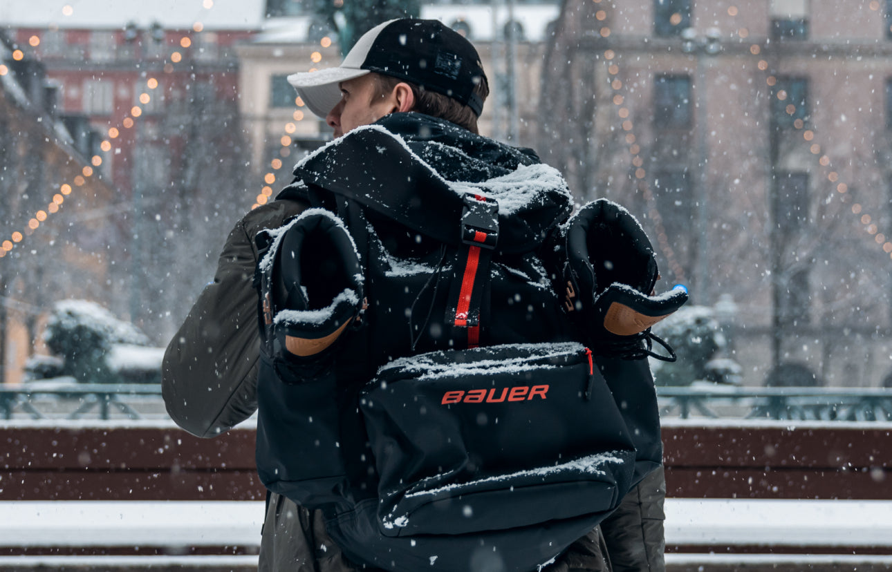 following a person walking outside in a winter city wearing a backpack with hockey skates