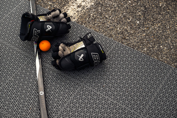 hockey gloves, stick, and street hockey ball lying on top of grey training tiles
