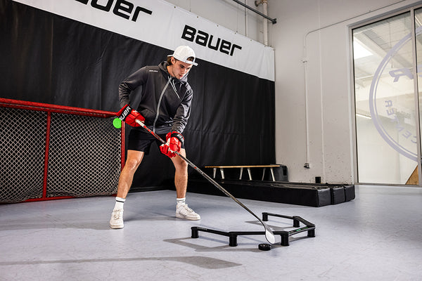 Jack Hughes practicing stickhandling in a gym with bauer logos on the walls