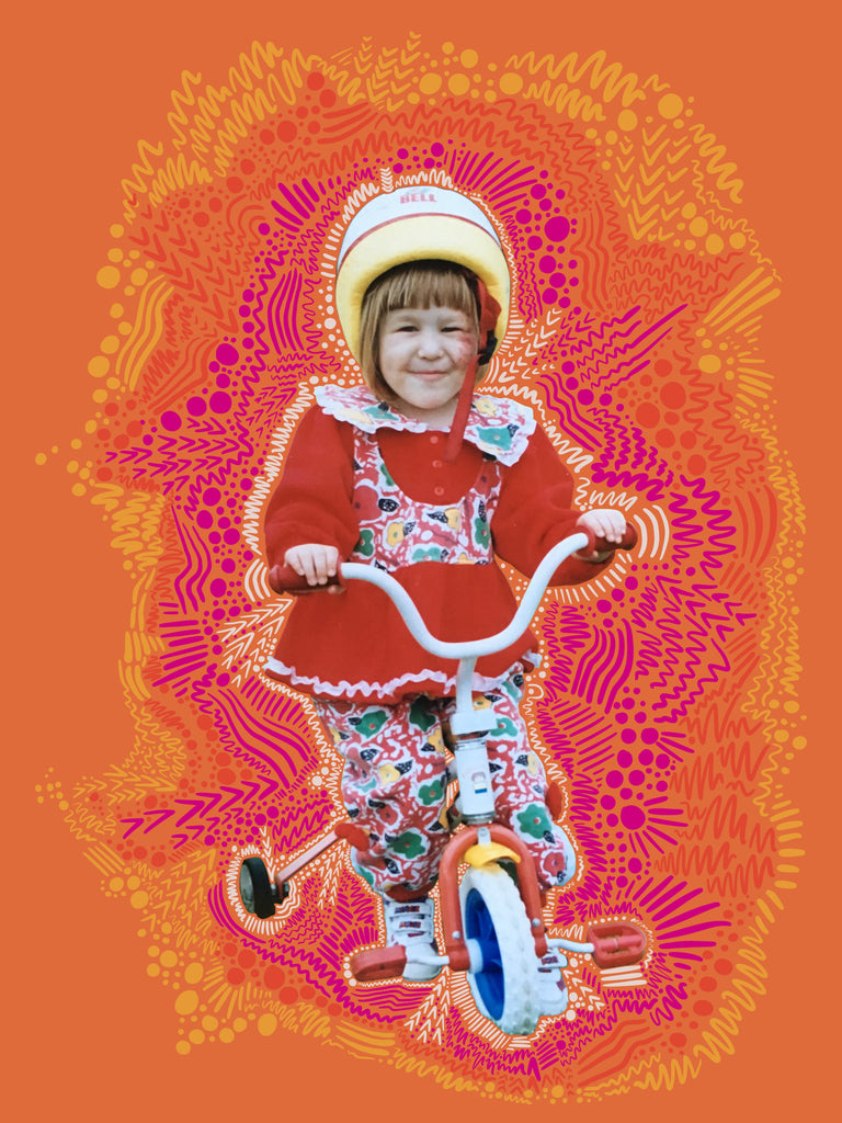 Digital collage. A little girl sits on a bike with training wheels and a helmet on. She has a birthmark on her face, a dark blonde bob, red/patterned matching tunic/pants set and white sneakers on. Around her in rays are doodles that are white/hot pink/orange/yellow. The background is a darker orange. 