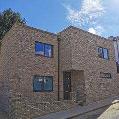 A square house with small windows in an art deco style, all clad in cream brick slips, with a small retaining wall at the front.