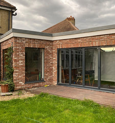 A flat roofed extension, clad in red reclaimed style blend 4 brick slips. There is a window in the short side of an L-shape, with bifolding doors on the long end.