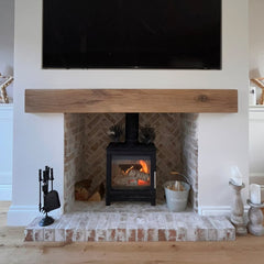 Beige and white brick slips come from an internal fire chamber out onto the hearth with a gas stove inside the chamber, and a wood beam above it.