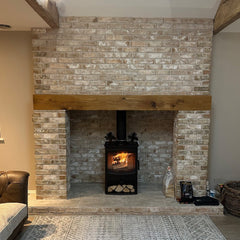 A large neutral brick slip fireplace, with a log burning stove inside, and a wooden beam across the top of the opening.