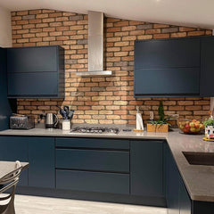A navy handleless kitchen with a grey work surface. Reclaimed style brick slips are behind the units in a sloping roofed extension.