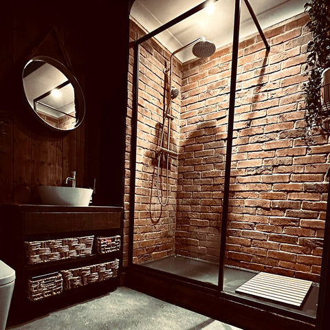 Red brick slips in a shower cubicle. A mirror and sink are to the right of the cubicle itself.