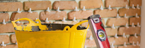 A bucket and spirit level in front of a part installed brick slip wall.