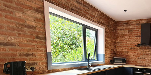 A window with trim around it surrounded by a brick slip wall in a kitchen.