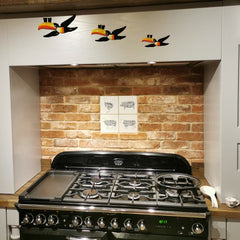 Red Brick Slip Hob backsplash with 4 ceramic tiles centrally, above a stove. 3 toucans are affixed to the wall above.