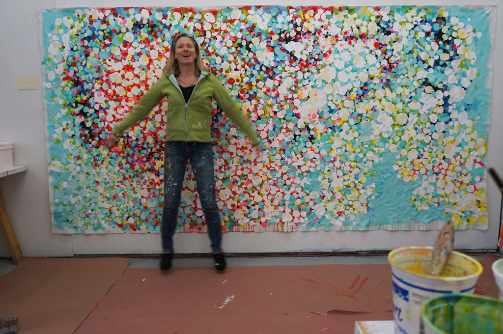 Abstract artist, Claire Desjardins, in front of her large, colourful painting.