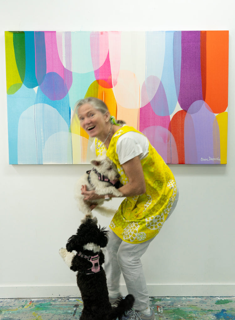 Abstract artist, Claire Desjardins, plays with her two dogs in her studio, in front of one of her colourful paintings.