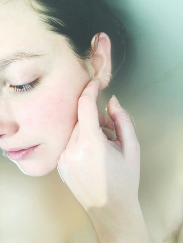 A woman's face partially submerged in water, gently touching her cheek.