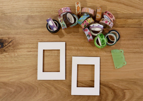 A grouping of 20 various wash tape at the top middle to right. Below sit two flat white outlet covers  on a light wooden coffee table