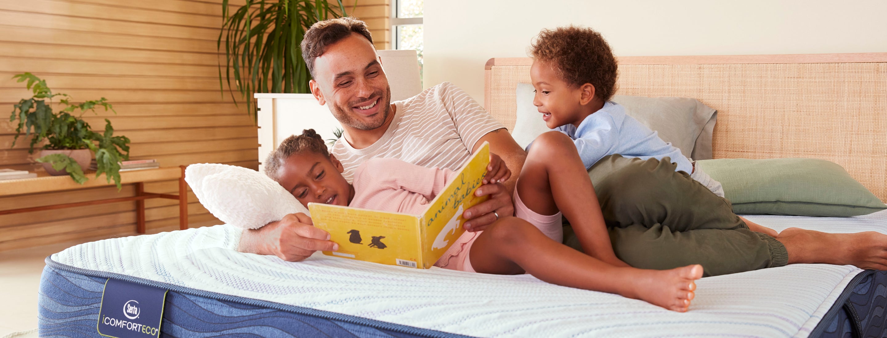 Dad and his two kiddos laying on top of an unmade Serta iComfortEco Mattress reading a book