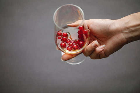 a lady's hand, holding a wine glass that has cranberries and wine