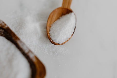 a wooden spoon with sugar crystals, placed on a white marble 