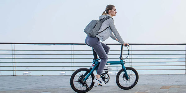 Una donna in sella a una bici elettrica pieghevole con una borsa sulle spalle