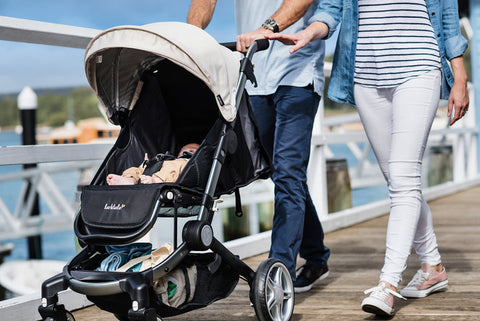 Two adults walking over a bridge with their baby buckled into a lightweight stroller