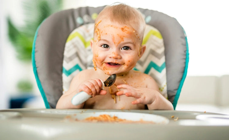 Baby playing with messy food on a high chair, a must-have baby registry item
